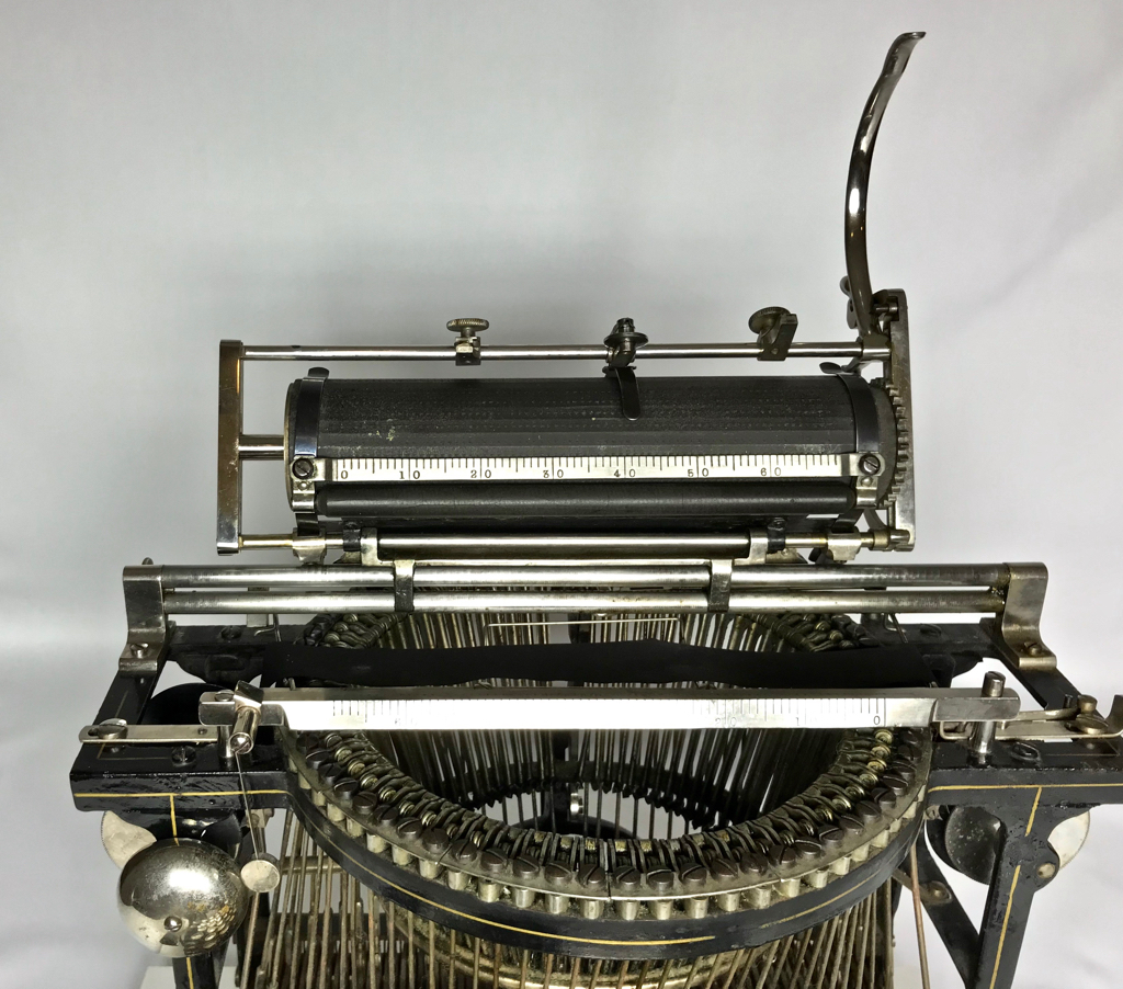 Since the letters are typed on the bottom of the platen, the operator had to rotate the entire carriage mechanism upward with the visible long lever to see what had been written.